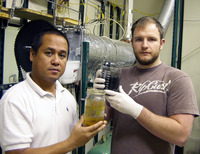 CE-CERT development engineers Junior Castillo (left) and Eddie O’Neil (right) display the results of the steam hydrogasification process that converts urban waste feedstock (rear container) into clean synthetic diesel fuel (foreground container). The fuel was produced in the lab-scale reactor behind them.